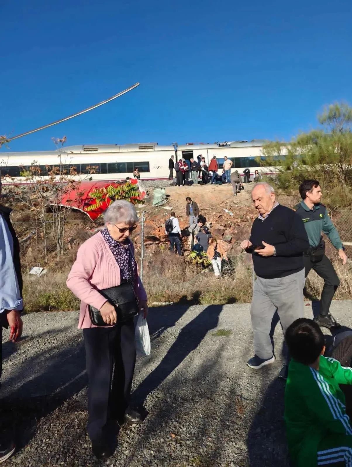 Pasajeros evacuados junto a la vía tras la colisión de trenes cerca de Urda, Toledo; al fondo, un tren AVE y restos de un vagón