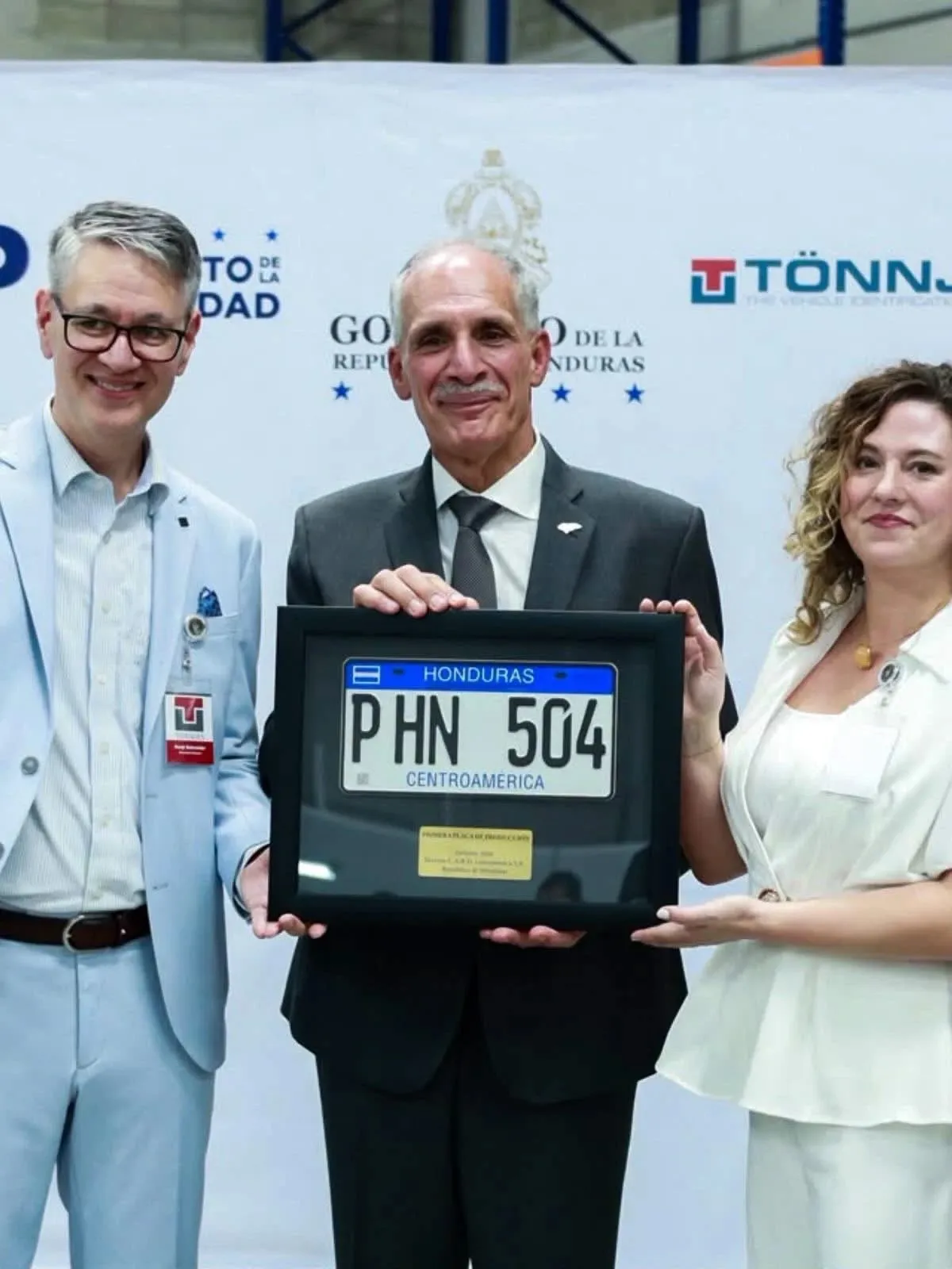 Representantes del Gobierno de Honduras y de la empresa Tönnjes sostienen enmarcada la primera placa de producción, con la matrícula «P HN 504»
