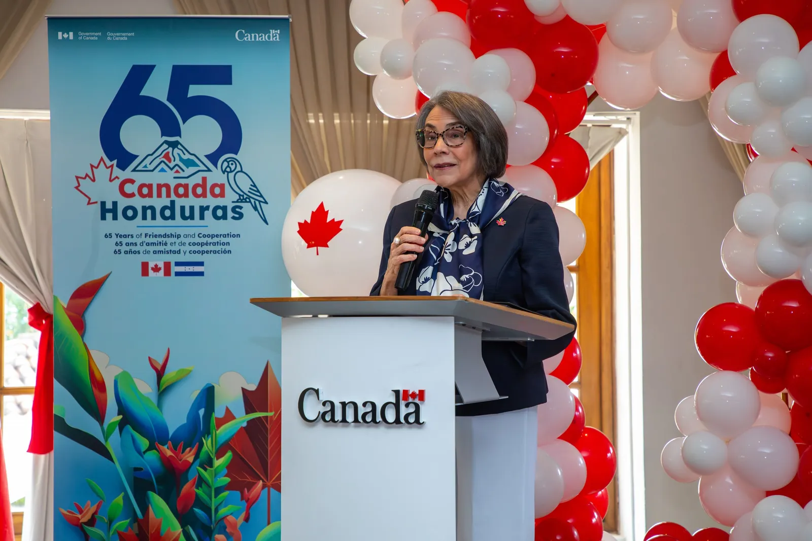 Una oradora habla desde el atril de Canadá, junto al cartel por los 65 años de amistad y cooperación entre Canadá y Honduras