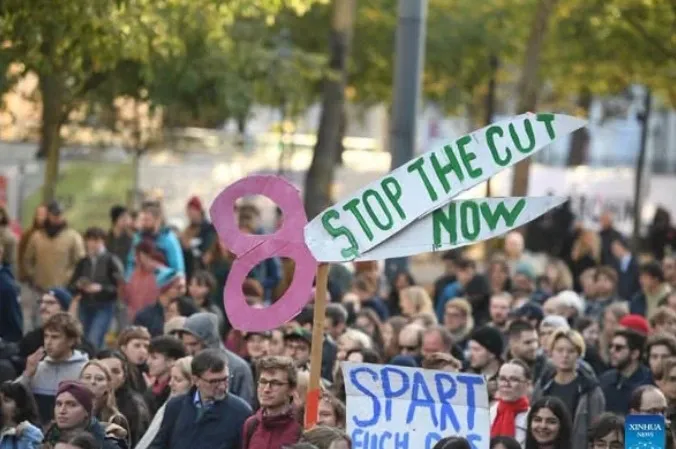 Manifestantes en Viena con una pancarta en forma de tijera que dice «Stop the cut now»