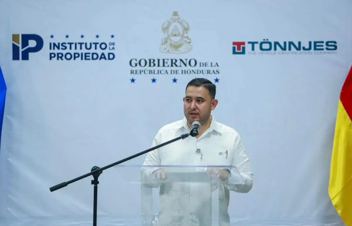 Un funcionario habla desde el podio en el arranque de la producción de placas, frente a los logos del Instituto de la Propiedad, el Gobierno de Honduras y Tönnjes